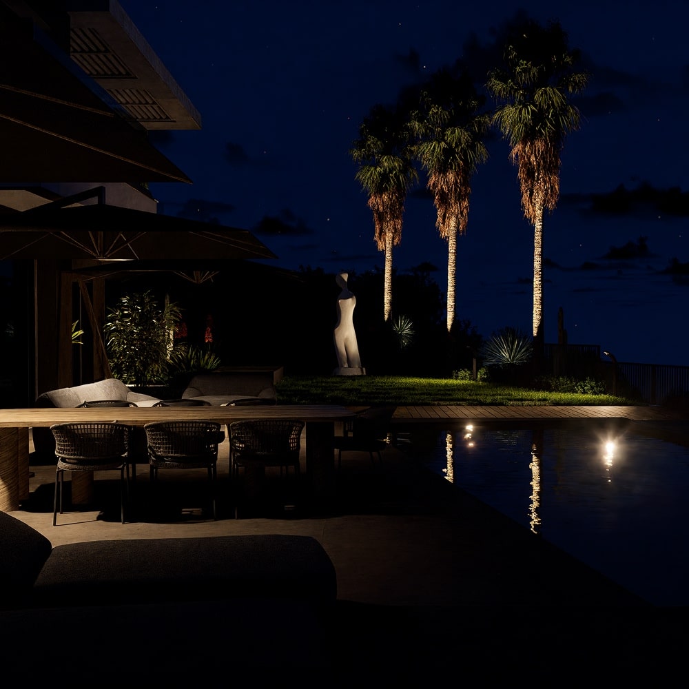 Terrasse moderne de nuit avec piscine, mobilier de jardin élégant et palmiers éclairés sous un ciel étoilé.