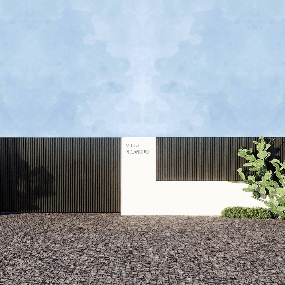 Mur minimaliste Villa Misandro avec clôture noire, plantes grasses et pavés sous un ciel bleu aquarelle.